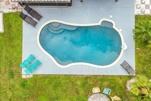Eine Vogelperspektive auf ein Schwimmbecken mit einer Liegefläche, umgeben von Rasen und einigen Liegestühlen.