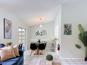 Ein modernes Wohnzimmer mit einer Couch, einem Esstisch, Stühlen, einer Küchenzeile mit Bar und einer großen Kühlpflanze.