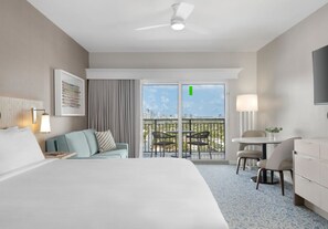 A hotel room with a bed, a desk, a chair, a balcony with a city view, and a ceiling fan. - Marriott's BeachPlace Towers 1 Guest Room,1 King, Sofa Bed, Balcony-Beach Vacay (Fort Lauderdale)