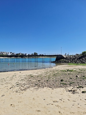 A beach with a rocky shoreline, a pier extending into the water, and houses in the background. - Family home, large garden, relaxation area, near the beach and downtown Audierne (Audierne)