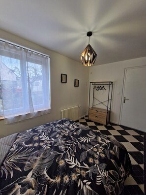 Et soveværelse med seng, radiator, pendel, garderobeskab og et vindue med gardiner.