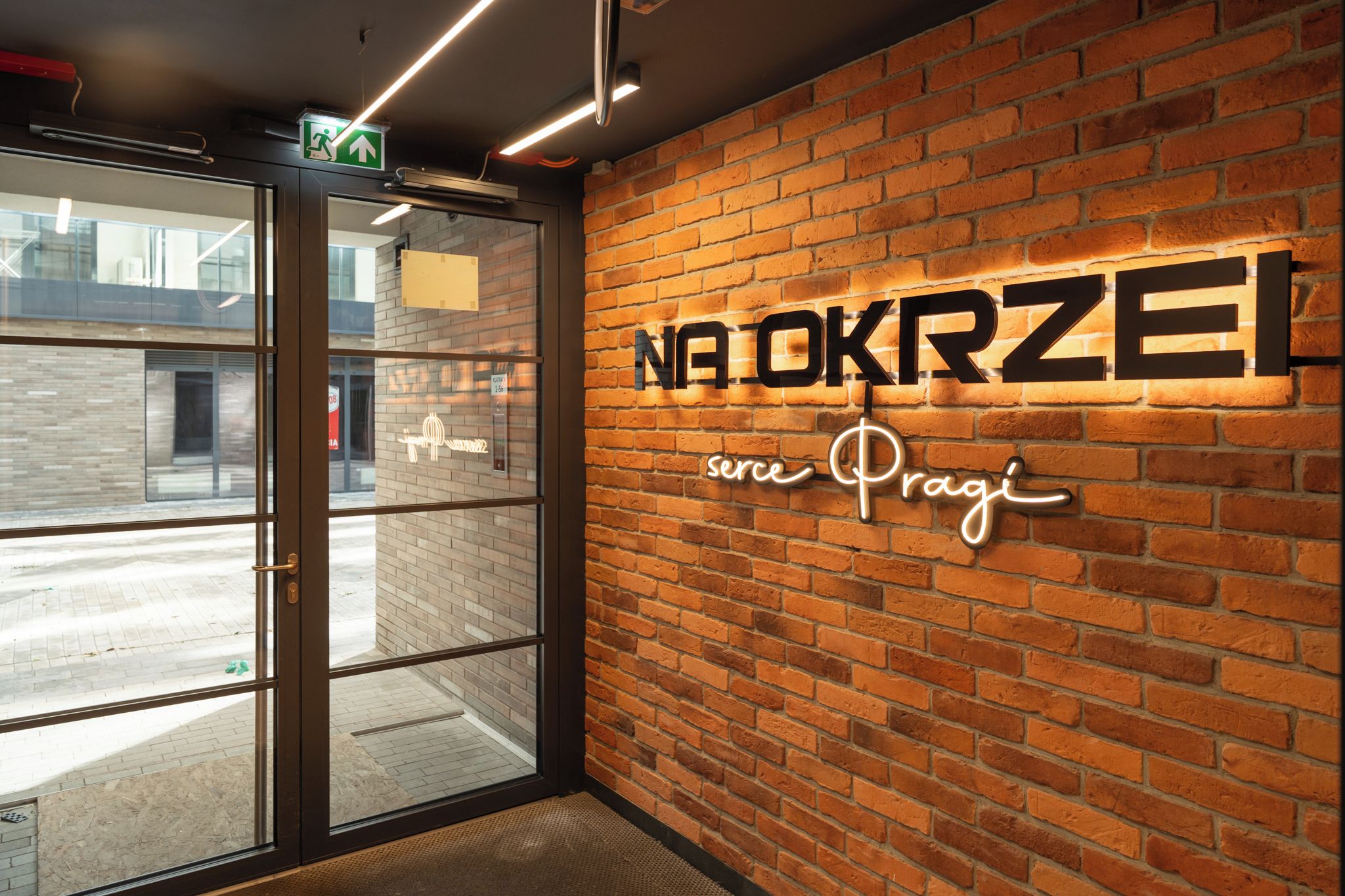 A brick wall with illuminated signage reading 'NA OKRZEL' and 'serve. Prague'.
