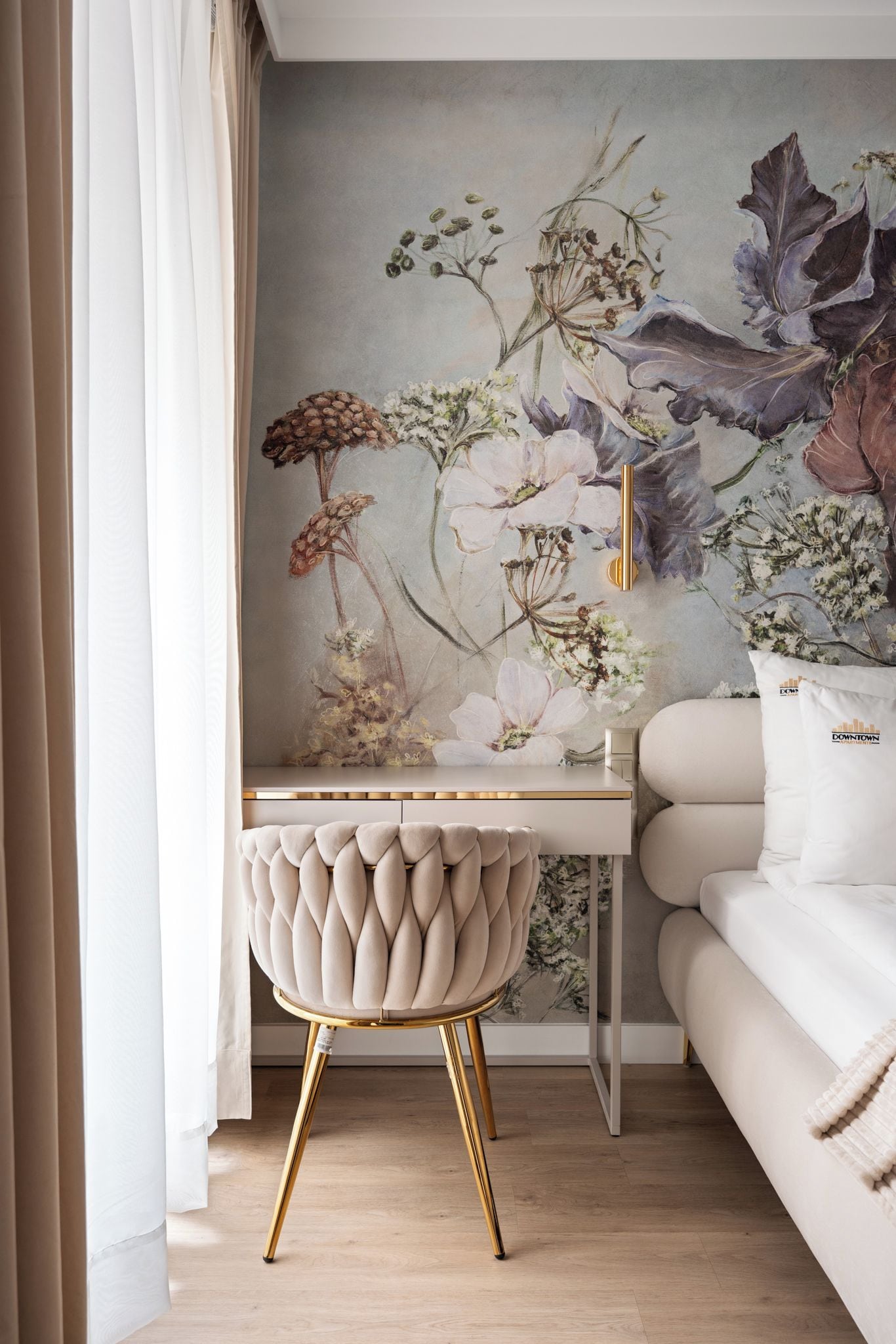 A room with a white sofa, a white desk with a gold chair, and a floral wall mural.