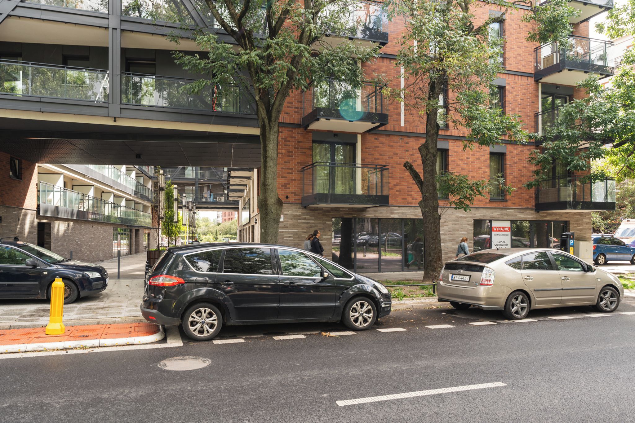 Une vue de rue avec un bâtiment moderne doté d’une façade en verre et d’une structure extérieure en briques.