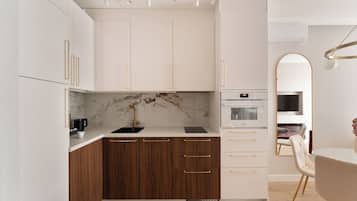 Una cocina moderna con armarios blancos, un salpicadero de mármol y un horno empotrado.