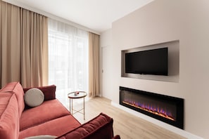 A modern living room with a red sofa, a flat-screen TV, and a fireplace. - Na Okrzei Riverside Suite Warsaw by Downtown Apartments (Warszawa)