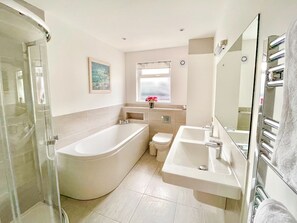 Un bany modern amb plat de dutxa de vidre, banyera independent, vàter i un lavabo amb rentapel.