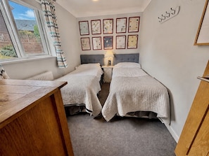 Een slaapkamer met twee bedden, een houten bureau, een raam met gordijnen en een wand met ingelijste foto's.