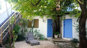Un espace extérieur abrité, aménagé avec des sièges et une chaise, entouré de plantes en pot et d’un escalier.