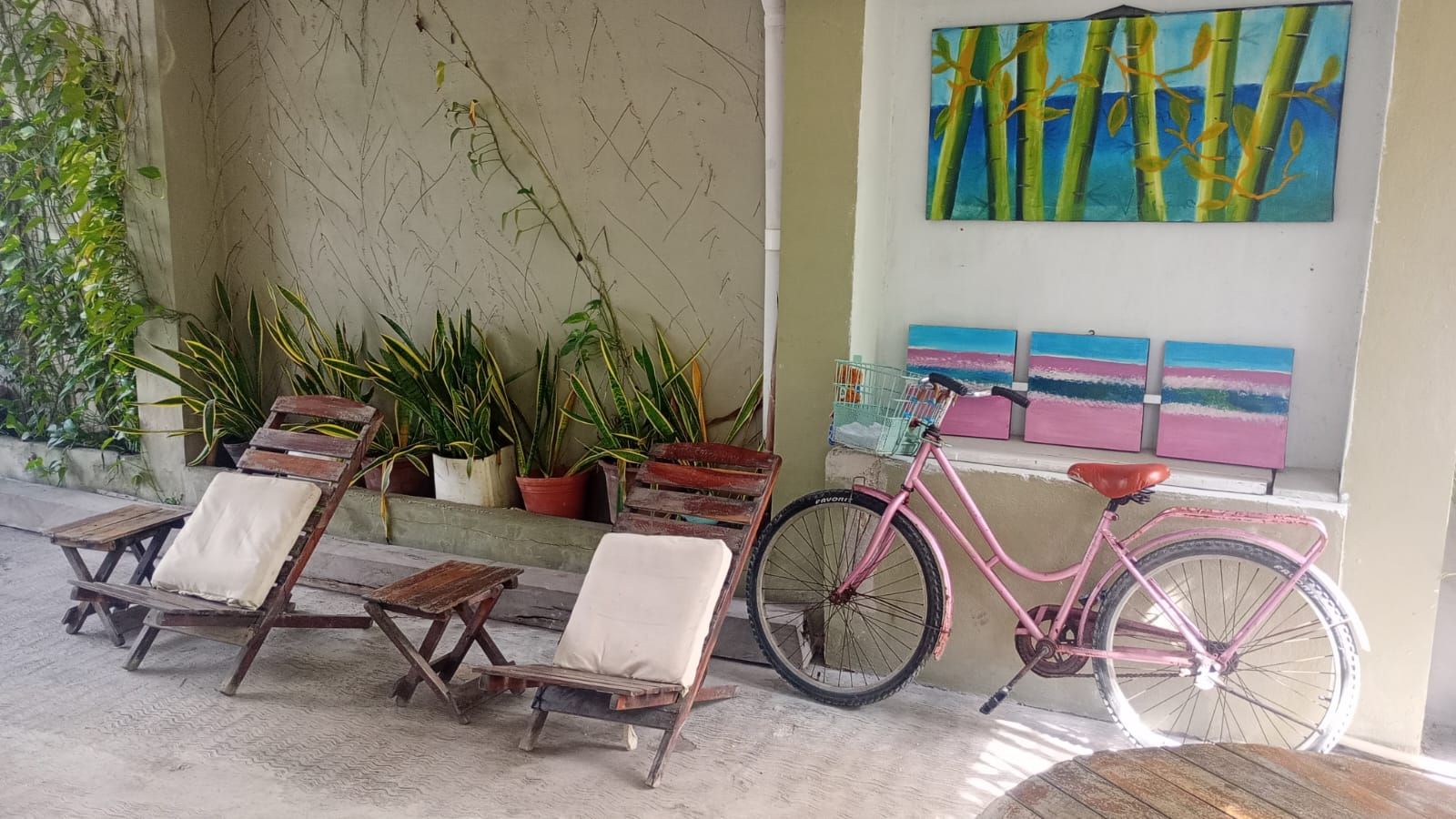 A covered outdoor seating area with wooden chairs and a pink bicycle.