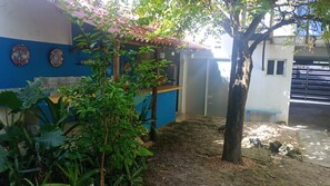 Une cour avec un bâtiment bleu, un arbre et une porte.