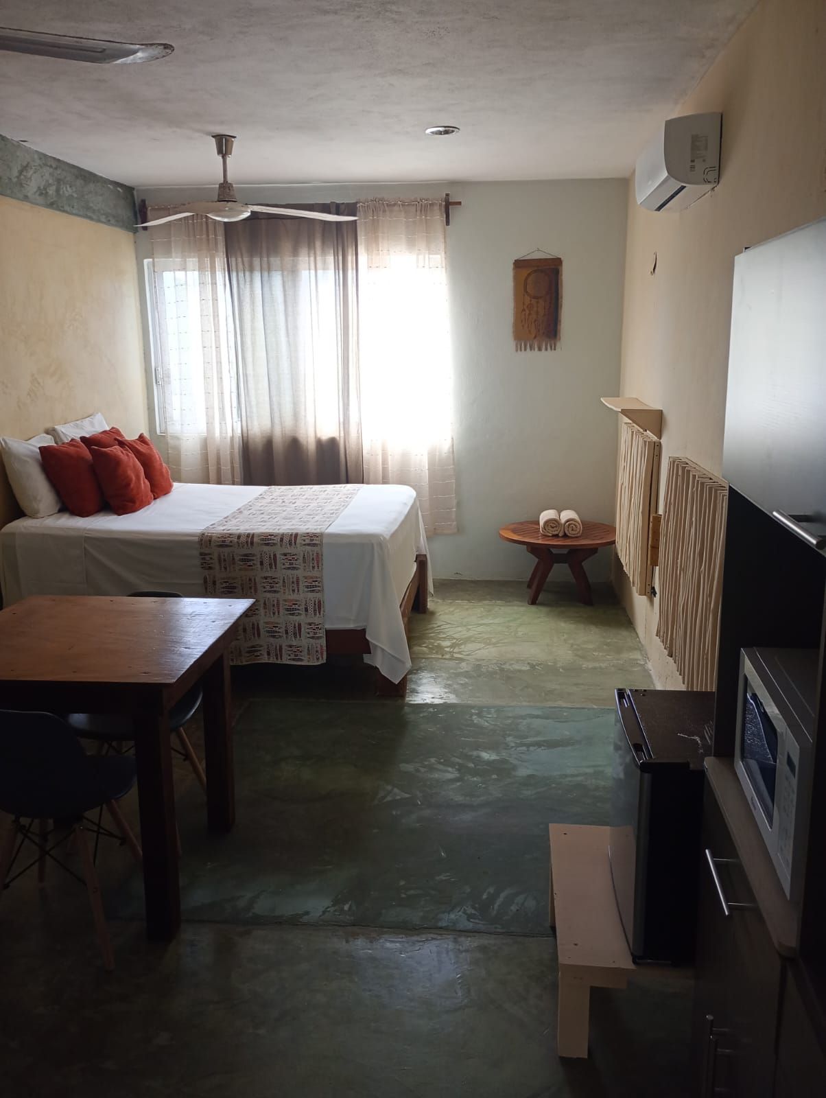 A room with a bed, a table, a chair, a small round table with a towel, and a TV.