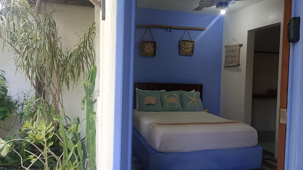 A bedroom with a bed, a blue wall, and a hanging plant.