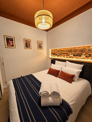 Een opgemaakt bed met een gestreept dekbed, kussens en opgerolde handdoeken.