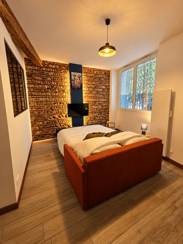 Een slaapkamer met een stenen muur, een bed, een televisie en een raam.