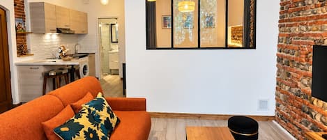 Ett modernt vardagsrum med en soffa, ett soffbord i trä och en matplats med en tegelvägg och ett stort fönster.