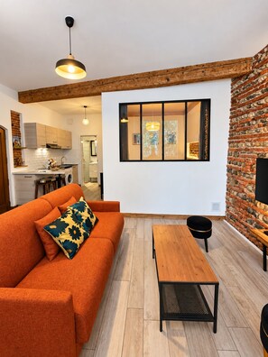 Een moderne woonkamer met een bank, een houten salontafel en een eethoek met een bakstenen muur en een groot raam.