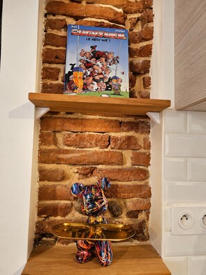 A brick fireplace with a shelf holding a rugby-themed book and a colorful bear figurine. - Vrbo Property (Toulouse)