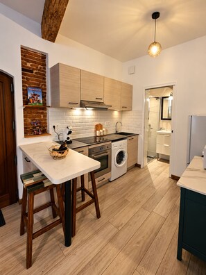 Een moderne keuken met houten kasten, een inbouwoven, een wasmachine en een eethoek met krukken.