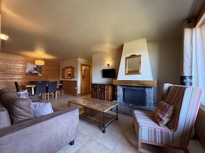 Ein Wohnzimmer mit Sofa, Sessel, Couchtisch, Kamin und Essbereich.