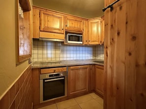 A kitchen with wooden cabinets, a microwave, an oven, and a tiled backsplash. - 50m from ski slopes, sauna, hammam, balcony, fireplace or stove, tv, ski locker, 73m², La Plagne (La Plagne)