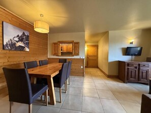 A dining area with a wooden table and chairs, a kitchen with wooden cabinets, and a television on a cabinet. - 50m from ski slopes, sauna, hammam, balcony, fireplace or stove, tv, ski locker, 73m², La Plagne (La Plagne)