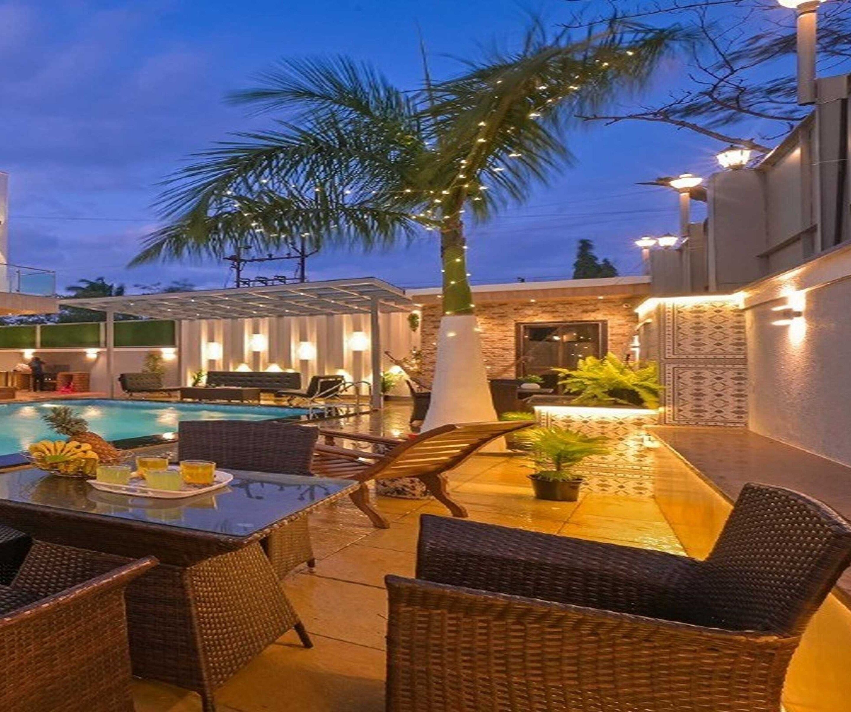 A poolside area with wicker furniture, a dining table with drinks, and a palm tree.