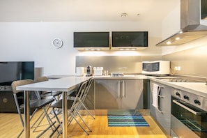 A compact kitchen with a microwave, oven, and a small dining area with a table and chairs. - Le Nid Grenoblois - Appart dans Grenoble pour 4 (Grenoble)