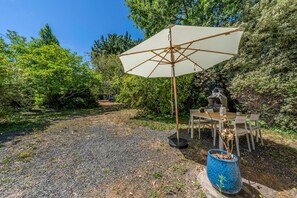 A gravel patio with a wooden table and chairs, a white umbrella, and a blue planter. - Ty Arcouest - Proche de la plage (Ploubazlanec)