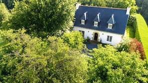 A white building with a dark roof, surrounded by dense green foliage. - Ty Arcouest - Proche de la plage (Ploubazlanec)