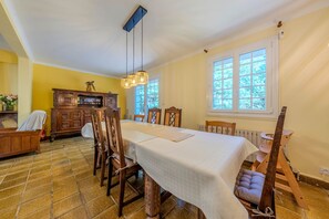 Un coin repas comprenant une longue table, des chaises, un buffet en bois et une fenêtre donnant sur un paysage verdoyant.