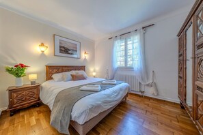 Quarto de hotel com uma cama grande, cabeceira de madeira, luminárias de cabeceira, uma janela com cortinas, um radiador e um guarda-roupa de madeira.