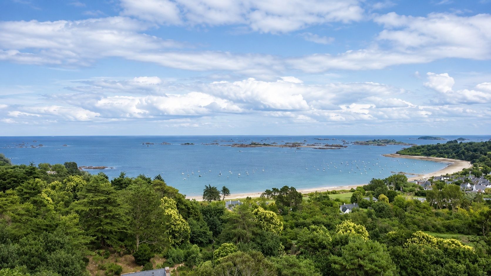 A coastal landscape with a beach, boats, and dense greenery.