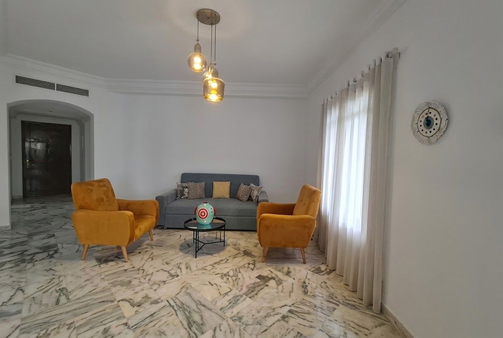 A living room with a sofa, two armchairs, a coffee table, and a decorative wall piece.