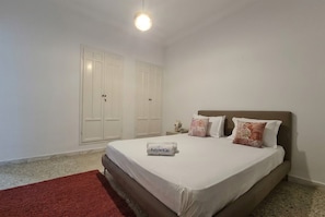 A bedroom with a bed, a red rug, white walls, and two white wardrobes. - sandra 19 (Gammarth)