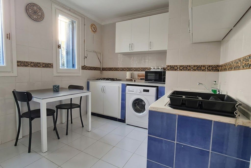 A compact kitchen with a dining table, chairs, a washing machine, and a microwave.
