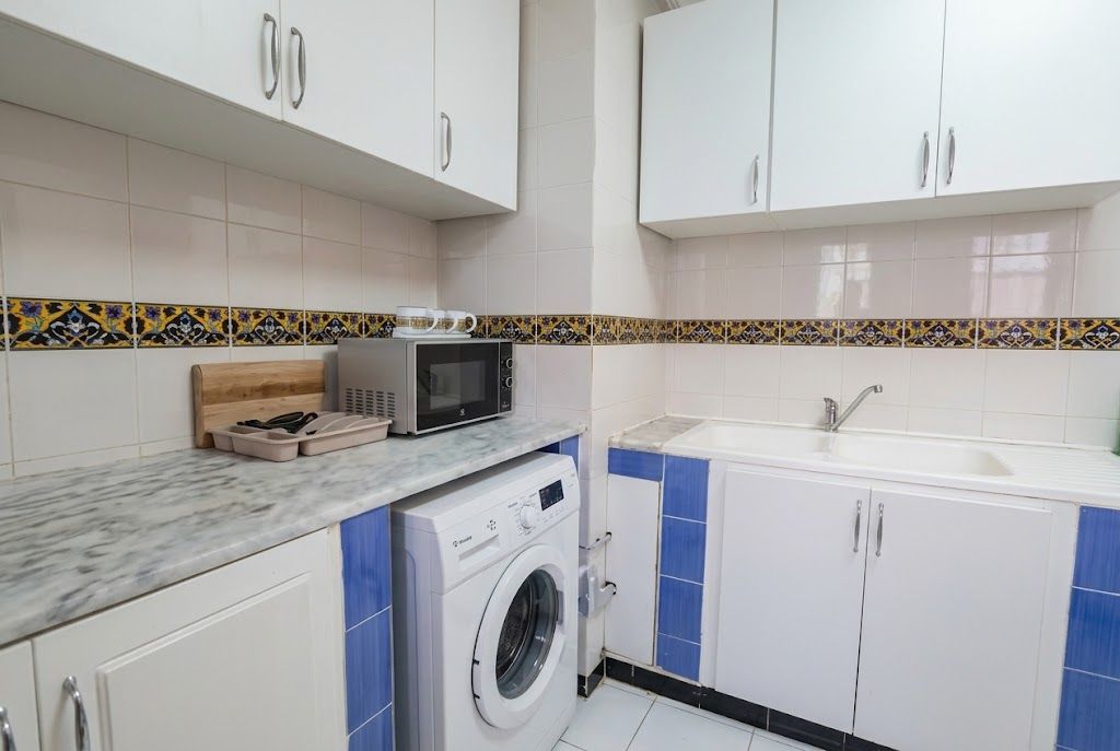 Una cocina compacta con armarios blancos, microondas, lavadora y pileta.