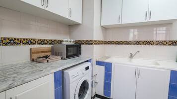 Una cocina compacta con armarios blancos, microondas, lavadora y pileta.