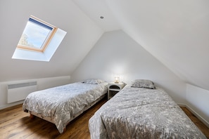 A small, sloped-roof bedroom with two beds, a skylight, a bedside table with a lamp, and a radiator. - Le Gite du Grand Parc - Jardin et parking privé (L'Oudon)