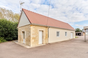 A single-story building with a sloped red roof, a small attached garage, and a visible antenna. - Le Gite du Grand Parc - Jardin et parking privé (L'Oudon)