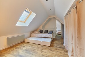 Quarto com teto inclinado, claraboia, cama com almofadas, radiador e chão de madeira.