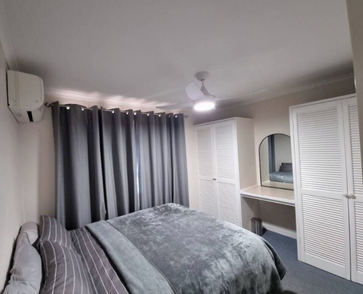 A bedroom with a bed, a ceiling fan, a wardrobe, and a mirror.
