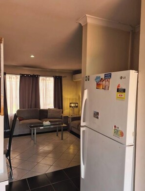 Ein gemütlicher Wohnraum mit einer Couch, einem Couchtisch, einem Kühlschrank und einer Lampe.