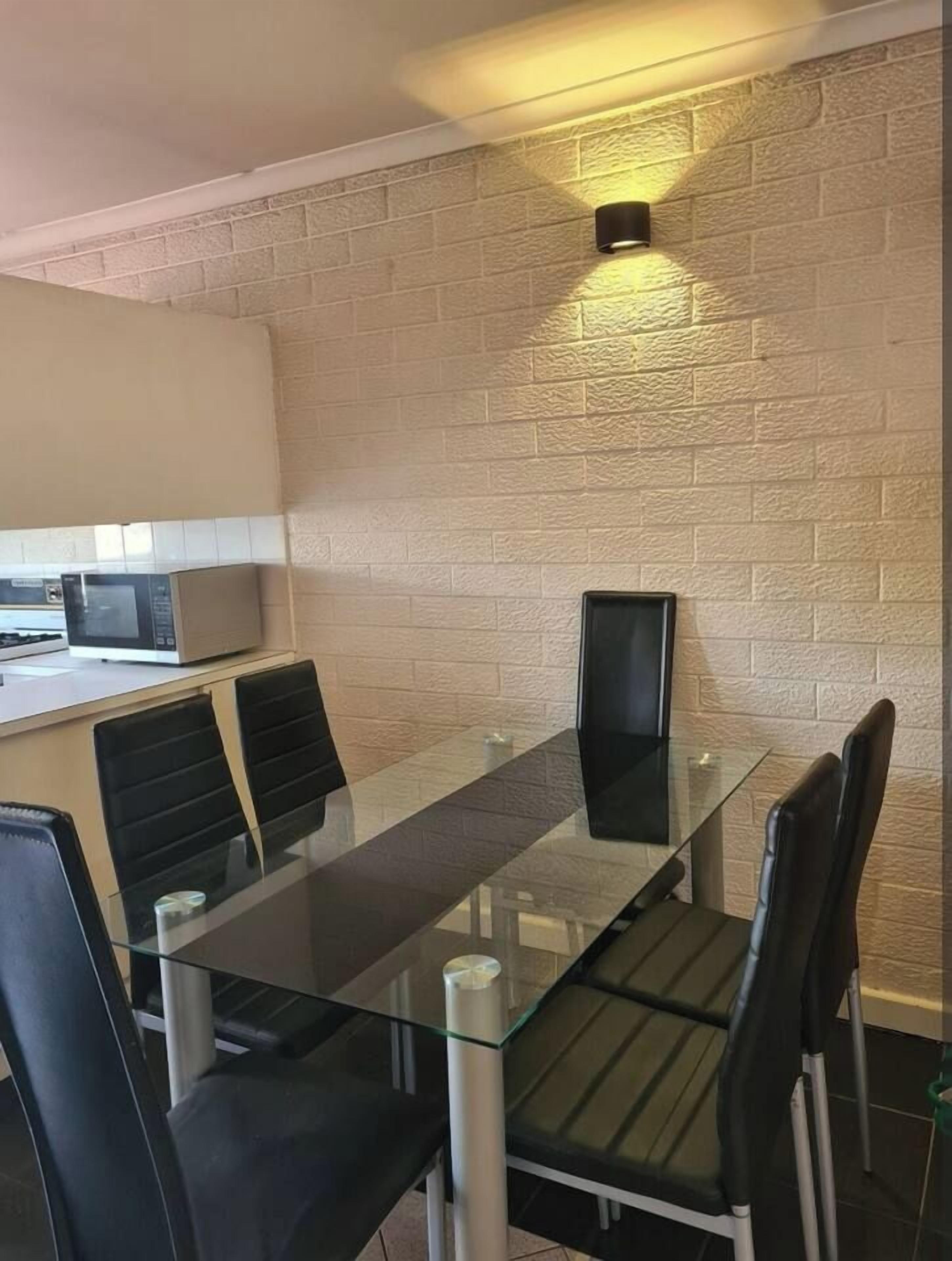 A modern kitchen with a microwave, a glass table with chairs, and a brick wall.