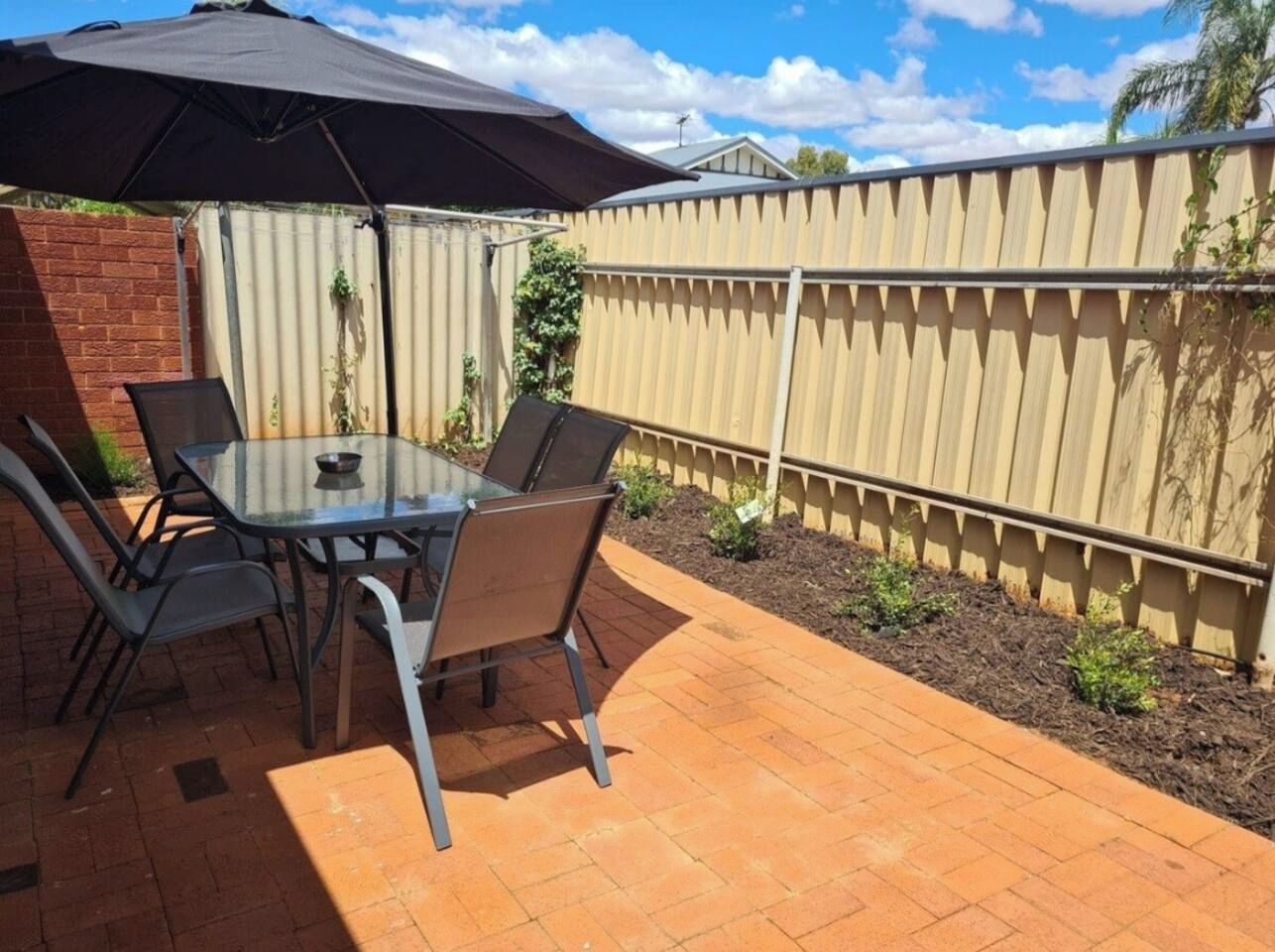 An outdoor patio with a table and chairs, a dark umbrella, and a wooden fence.