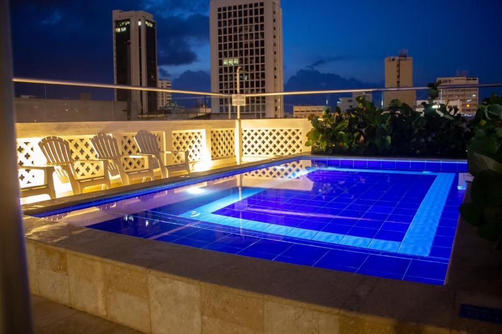 Une piscine sur le toit d’un immeuble, offrant une vue sur les bâtiments de la ville au crépuscule.