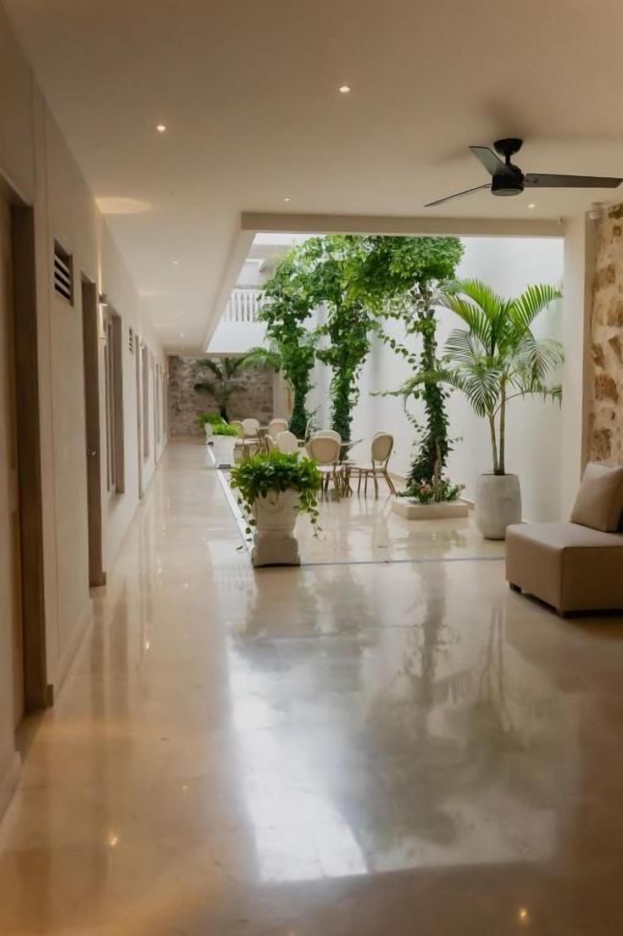 Un espacio interior amplio con piso pulido, ventilador de techo y zona de estar con mesas y sillas.