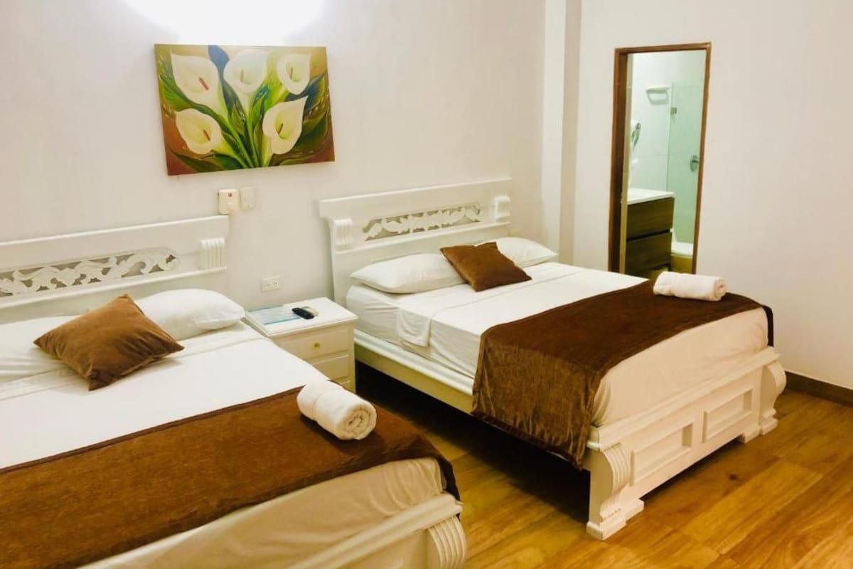 A hotel room with two beds, a painting on the wall, a mirror, and a wooden floor.