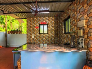 A kitchen area with a stone wall, a window, and a ceiling fan. - Classic Tanisha Guest House (Marmagao)