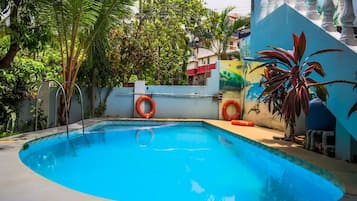 A swimming pool with a curved edge, surrounded by a white wall with a mural, and two orange lifebuoys attached to the wall.